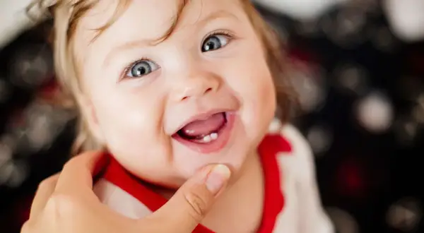 Ein Baby lächelt und zeigt stolz seinen ersten Zahn.