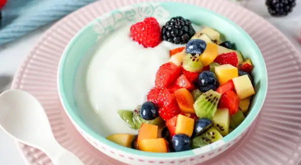 Ein Schüsselchen Joghurt mit frischem Obstsalat, perfekt für ein Kleinkind. Erdbeeren, Blaubeeren, Kiwi und Pfirsichstücke machen den Joghurt zum Genuss.