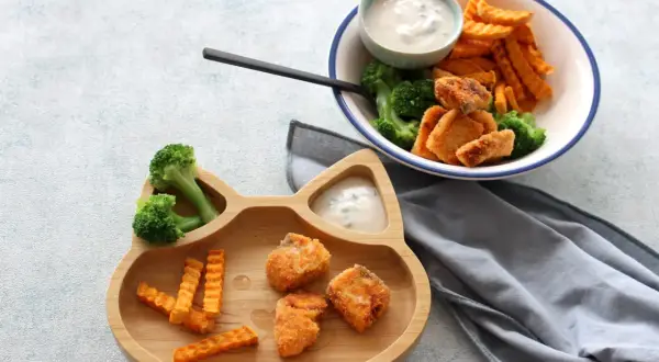 Fischstäbchen mit Brokkoli und Süßkartoffel-Pommes auf einem Katzen-Teller. Ab wann Fisch Baby essen darf, ist eine Frage für Eltern.