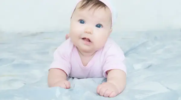 Blauäugiges Baby in rosa Strampler und Mütze. Mögliche kiss-syndrom symptome wie Kopfhaltung können hier nicht erkannt werden.