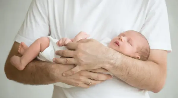 Ein Vater hält sein schlafendes Baby. Das Baby wedelt mit Armen und Beinen im Schlaf.