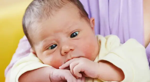Ein süßes Baby mit schielenden Augen, das nachdenklich auf seinen Fingern kaut.
