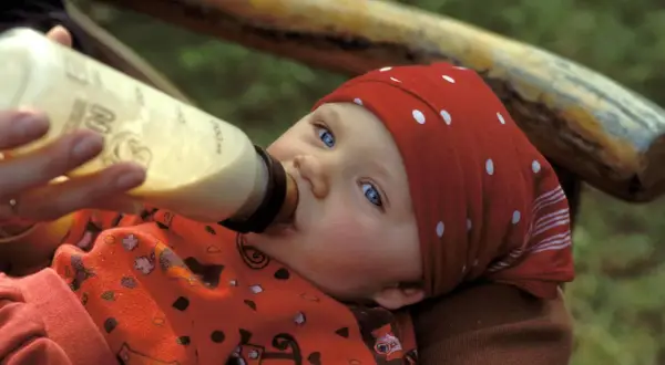 Ein Baby mit blauen Augen trinkt aus einer Flasche. Die Frage "wieviel sollten Kleinkinder trinken" beschäftigt viele Eltern.