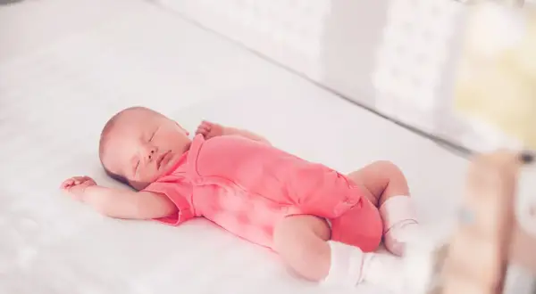 Ein schlafendes Baby in einem pinken Strampler streckt sich durch, während es in seinem Bettchen ruht.