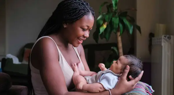 Eine junge Mutter lächelt ihr Baby an, das sie im Arm hält. Sie strahlt pure Energie in der Stillzeit aus.