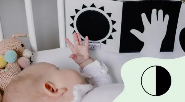 Ein Baby mit 2 Wochen erkundet mit seiner Hand ein Schwarz-Weiß-Buch mit Sonne und Hand.