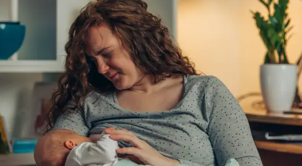 Mutter mit rissigen Brustwarzen stillt ihr Baby liebevoll, trotz des Schmerzes.
