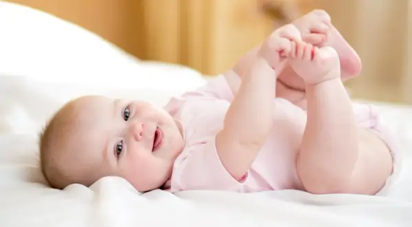 Ein lächelndes Baby von 8 Wochen liegt auf dem Rücken und spielt mit seinen Füßen.