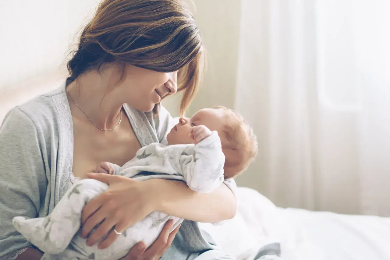 Mutter hält ihr Neugeborenes liebevoll im Arm. Ein Moment purer Zuneigung, eine stille Empfehlung für die innige Bindung zwischen Mutter und Kind.