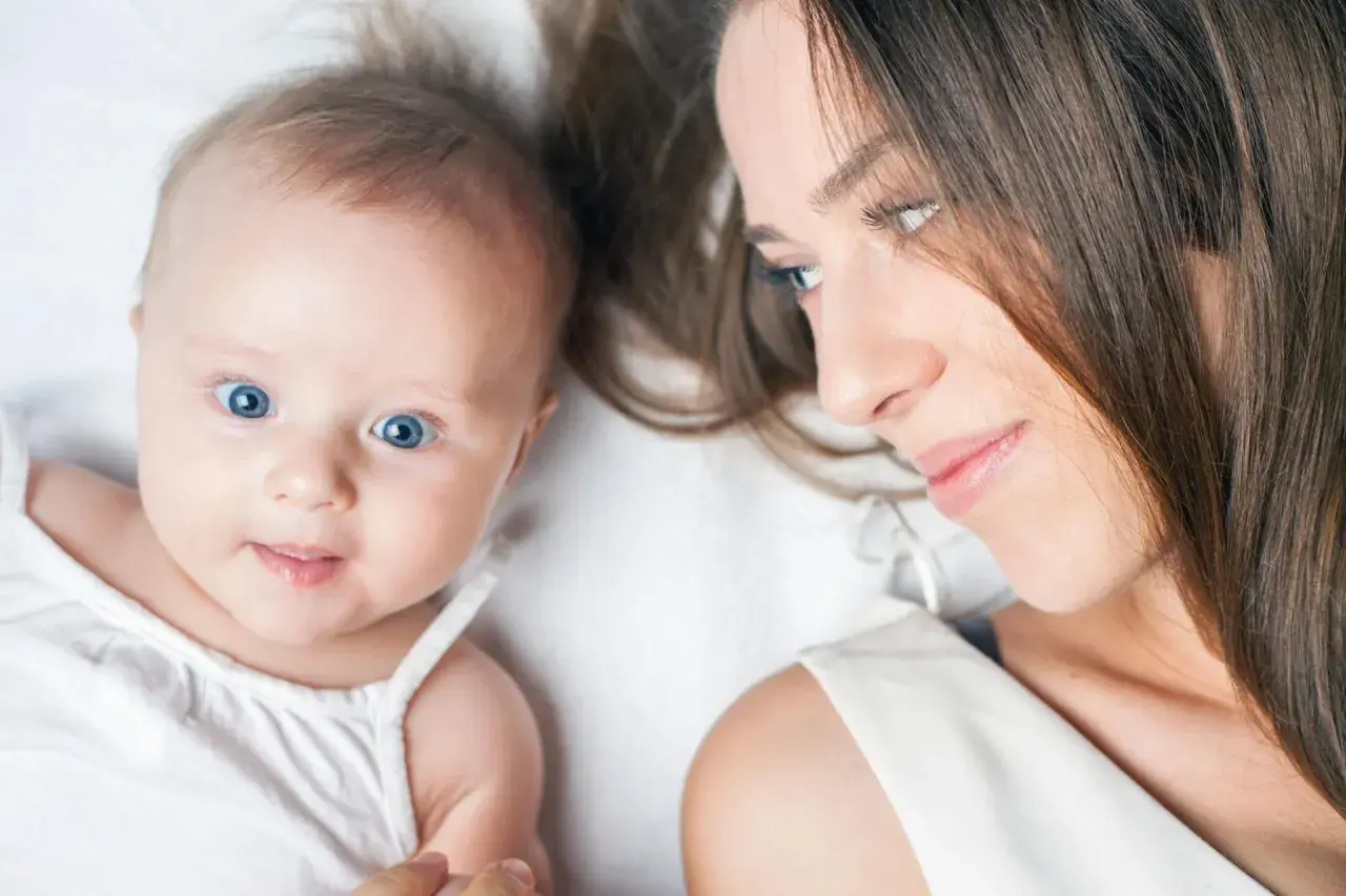 Ein Baby von 23 Wochen mit strahlend blauen Augen blickt neugierig in die Kamera, während seine Mutter es liebevoll ansieht.