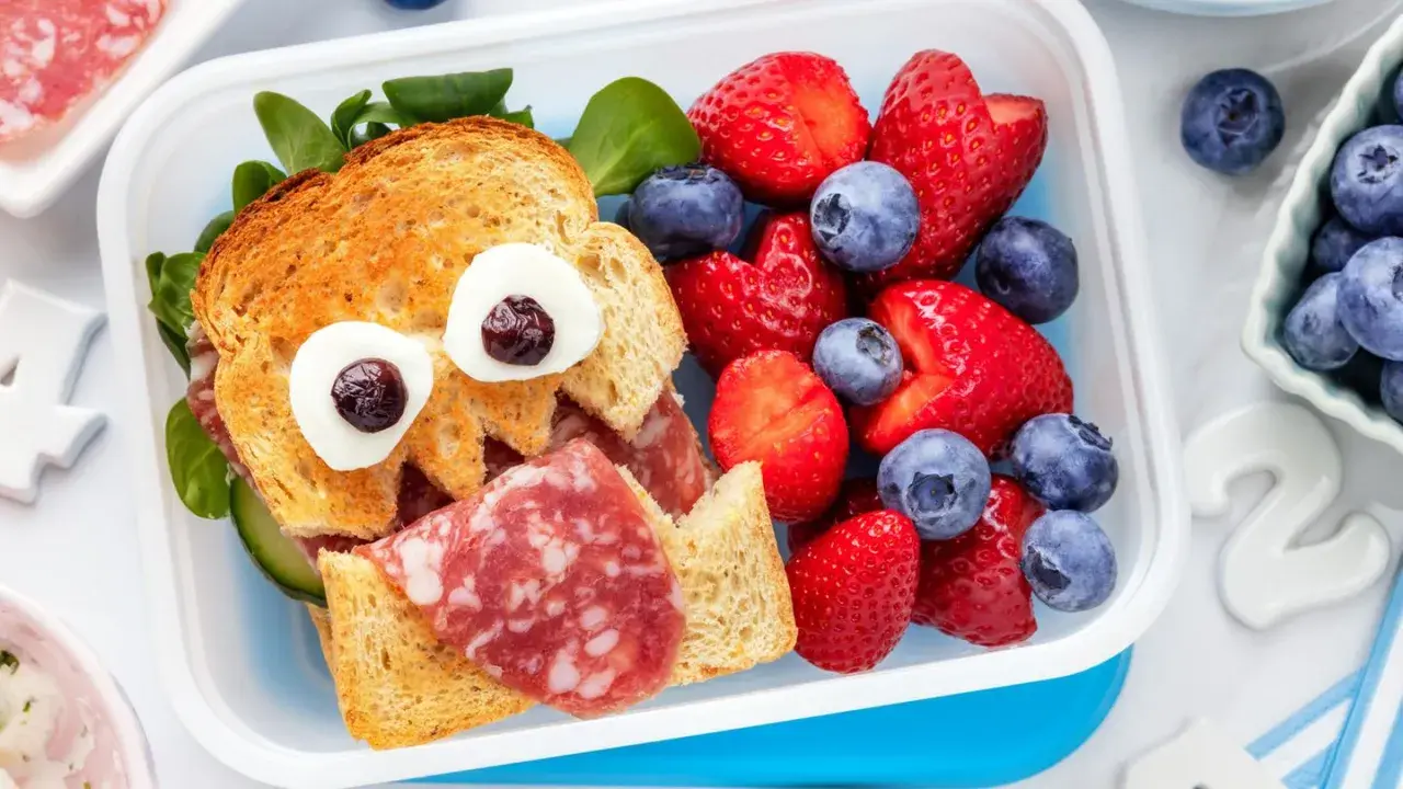 Ein lustiges Vesper-Essen Kita: ein Toast-Gesicht mit Wurst, Gurke und Beeren.