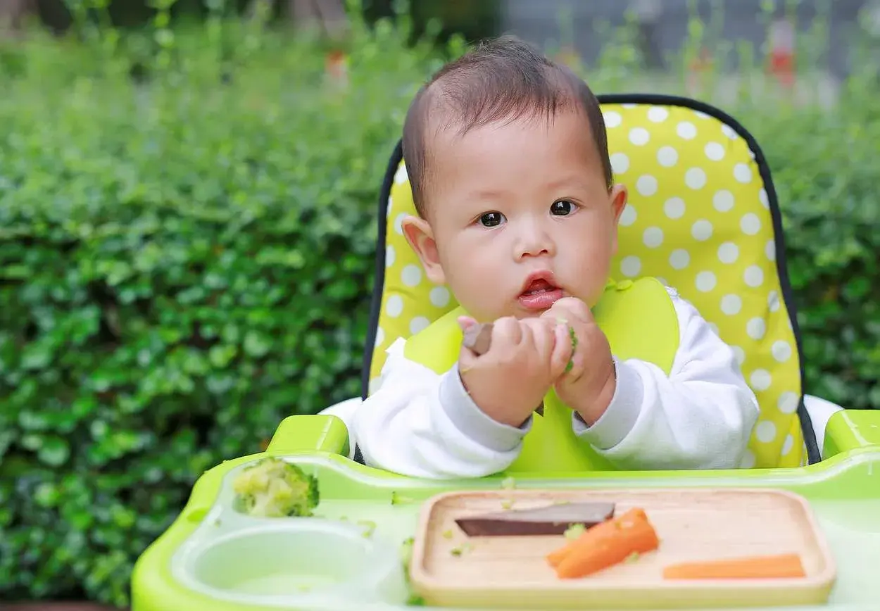 Ein süßes Baby isst im Hochstuhl. Der **Kalorienbedarf Baby 10 Monate** ist wichtig für seine Entwicklung.