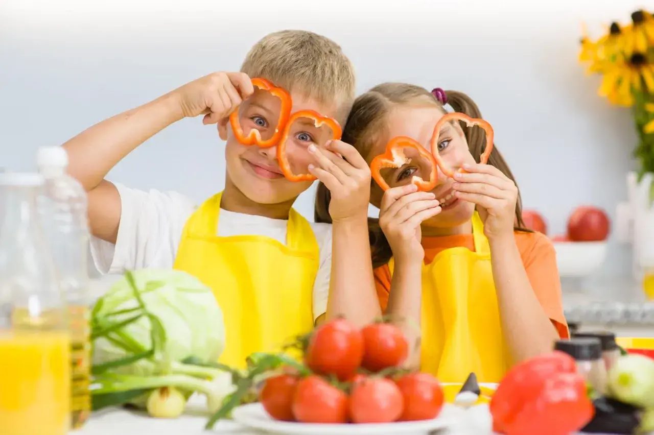 Zwei Kinder mit Paprikaringen vor den Augen, die Spaß beim Kochen haben. Gesunde Ernährung ist wichtig für den **Kalorienbedarf Kleinkind**.