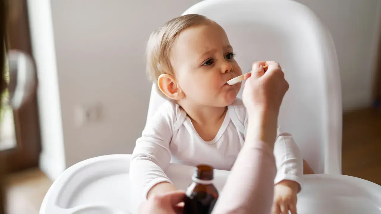 Ein Baby im Hochstuhl erhält Medikamente per Löffel. Die Eltern wechseln zwischen Ibuprofen und Paracetamol alle 4 Stunden, um Fieber zu senken.