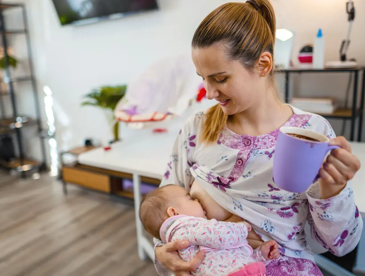Mutter stillt Baby, trinkt Kaffee. Mögliche baby koffein symptome beachten.
