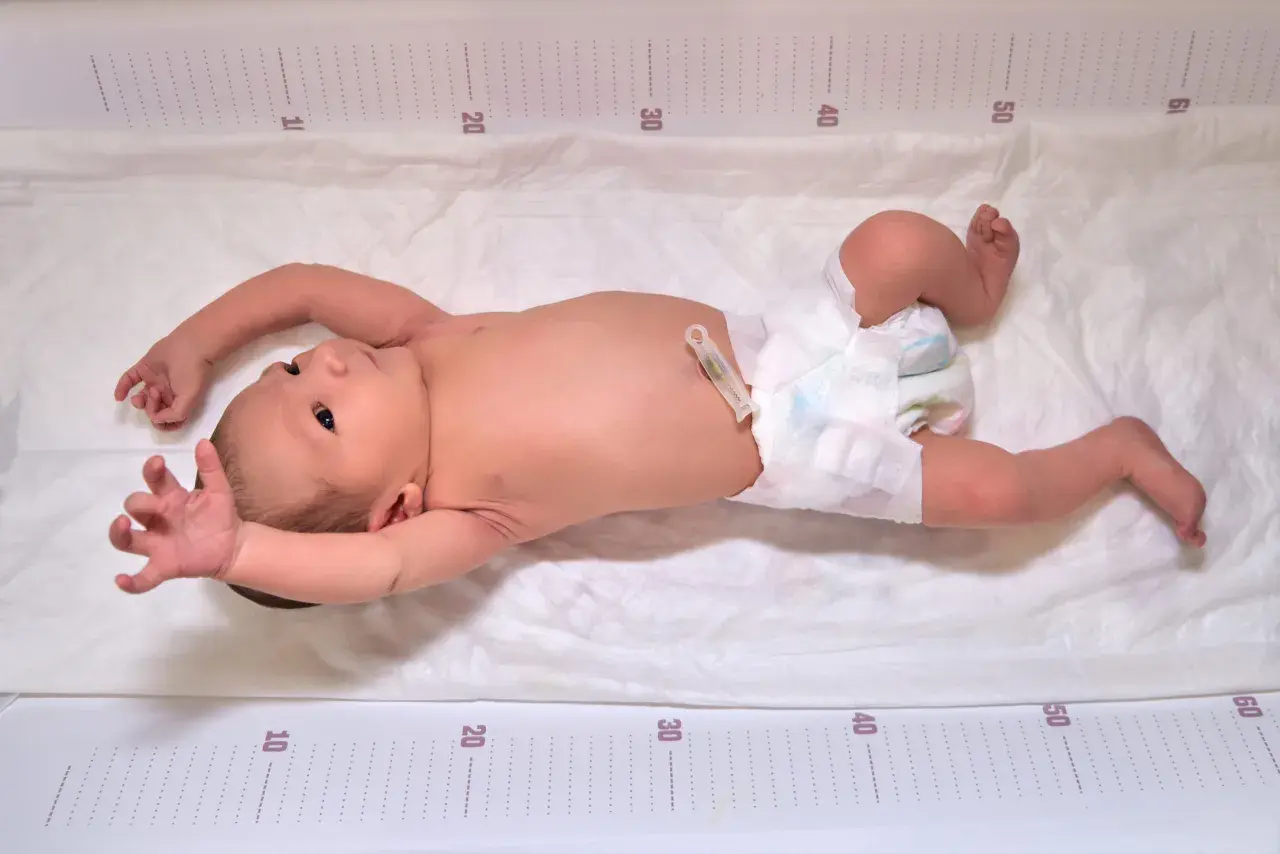 Neugeborenes Baby mit ausgestreckten Armen und Beinen, das den Suchreflex zeigt. Die Messskala am Rand deutet auf eine Größenmessung hin.