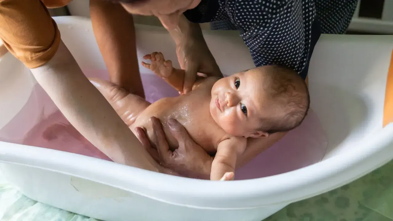 Ein Baby wird in einer Babybadewanne gebadet. Die Eltern prüfen die **Badetemperatur Baby**, damit es sich wohlfühlt.