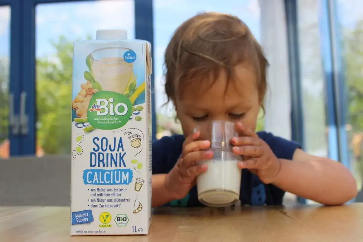 Ein süßes Kleinkind trinkt Soja Drink Calcium. Die Packung steht daneben.