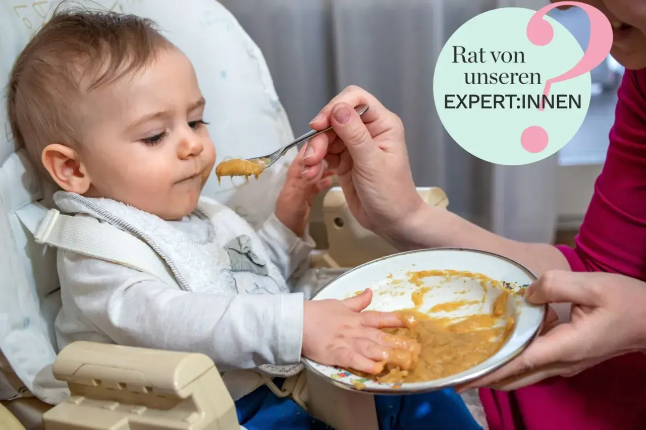 Ein Baby sitzt im Hochstuhl und bekommt Brei gefüttert. Die Hände des Babys sind voller Essen. Tipps für Baby essen von Expert:innen.