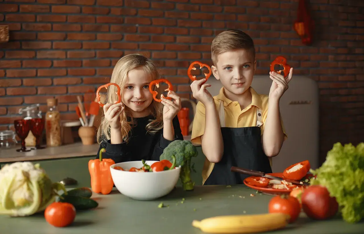 Zwei Kinder halten Paprikaringe hoch. Sie lernen, was muss man essen um zu wachsen: viel Gemüse!