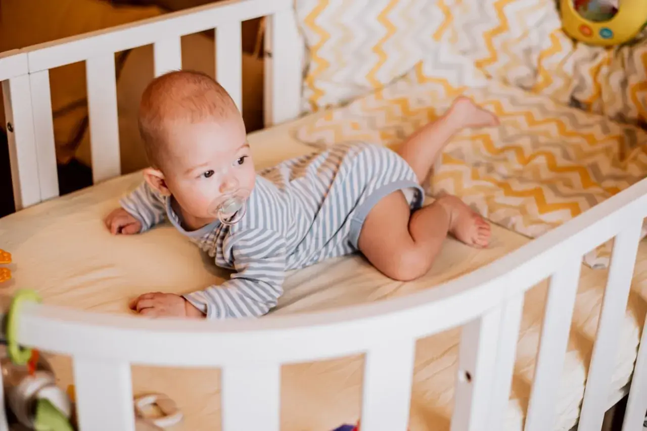 Baby liegt auf dem Bauch, der Schnuller im Mund. Es dreht sich noch nicht, aber die Beine sind schon aktiv.