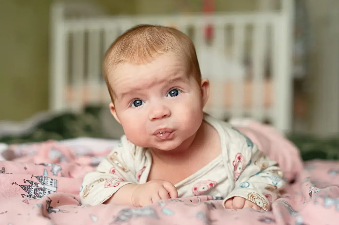 Baby mit blauen Augen liegt auf dem Bauch, sabbert und übt den 4 monats schub.