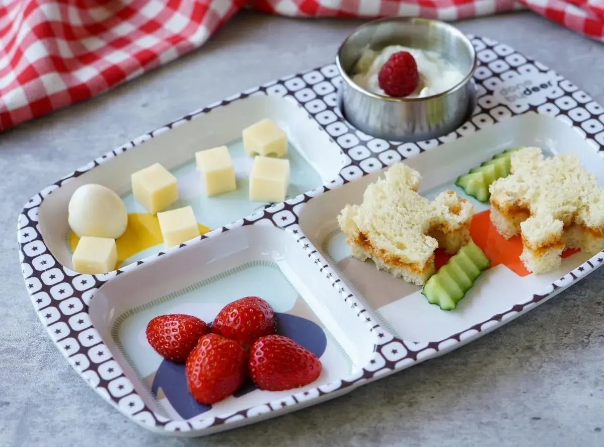 Leckeres Essen für ein Kleinkind (2 Jahre): Erdbeeren, Käsewürfel, ein Ei, Gurkenscheiben und ein süßes Sandwich.