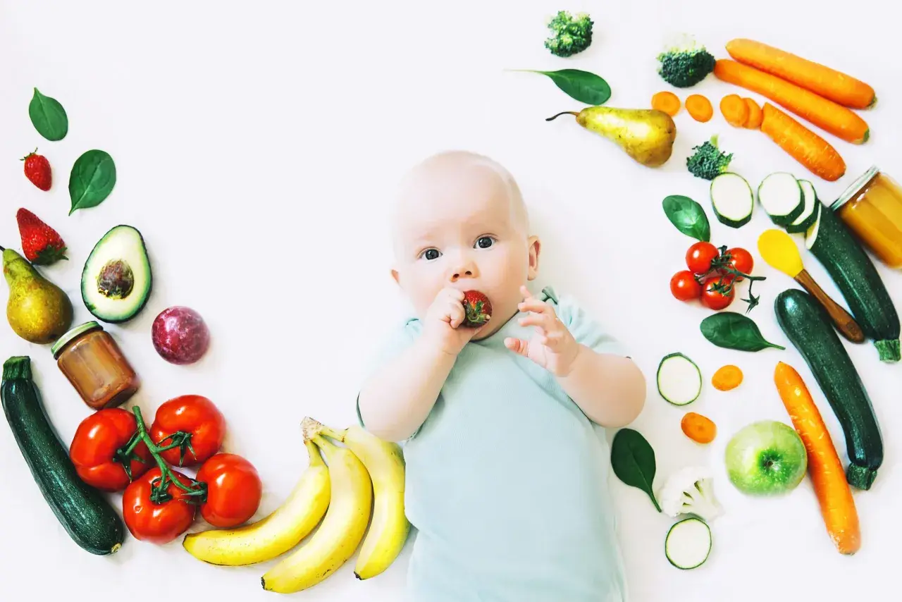 Baby mit Erdbeere im Mund, umgeben von Obst und Gemüse, das für die Lebensmittel und Milchbildung wichtig ist.