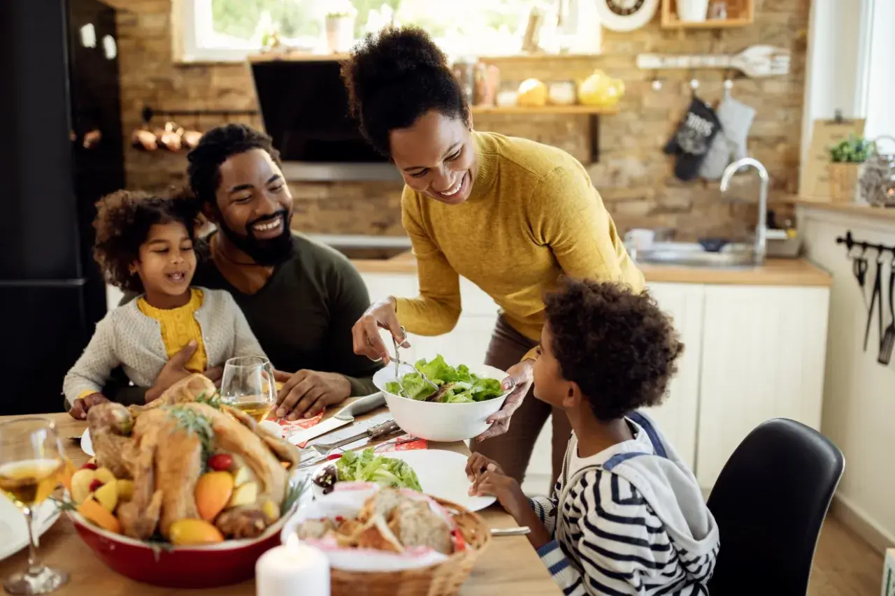 Familie am Esstisch, die ein Festessen genießt. Die Mutter reicht dem Sohn Salat, der wie mein Kind isst nicht 10 Jahre, hoffentlich probiert er.