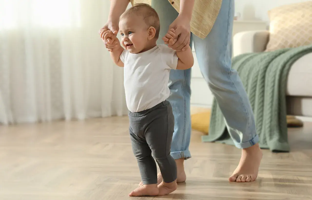 Ein Baby lernt laufen, gehalten von einer Person. Die ersten Schritte sind aufregend, wann stehen Babys?