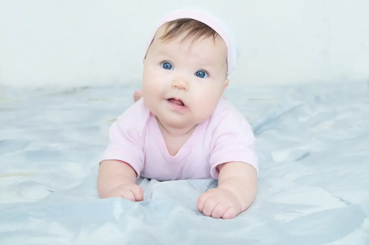 Blauäugiges Baby in rosa Strampler und Mütze. Mögliche kiss-syndrom symptome wie Kopfhaltung können hier nicht erkannt werden.