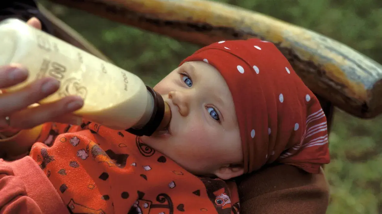 Ein Baby mit blauen Augen trinkt aus einer Flasche. Die Frage "wieviel sollten Kleinkinder trinken" beschäftigt viele Eltern.