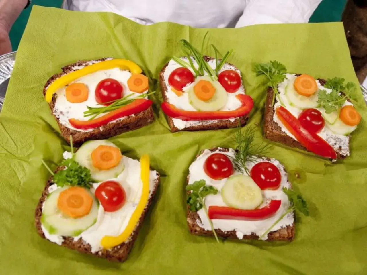 Lustige Gesichter auf belegten Broten: Fingerfood, das Kinder lieben. Bunte Gemüsesorten wie Paprika, Gurke und Karotte schmücken die Brotscheiben.