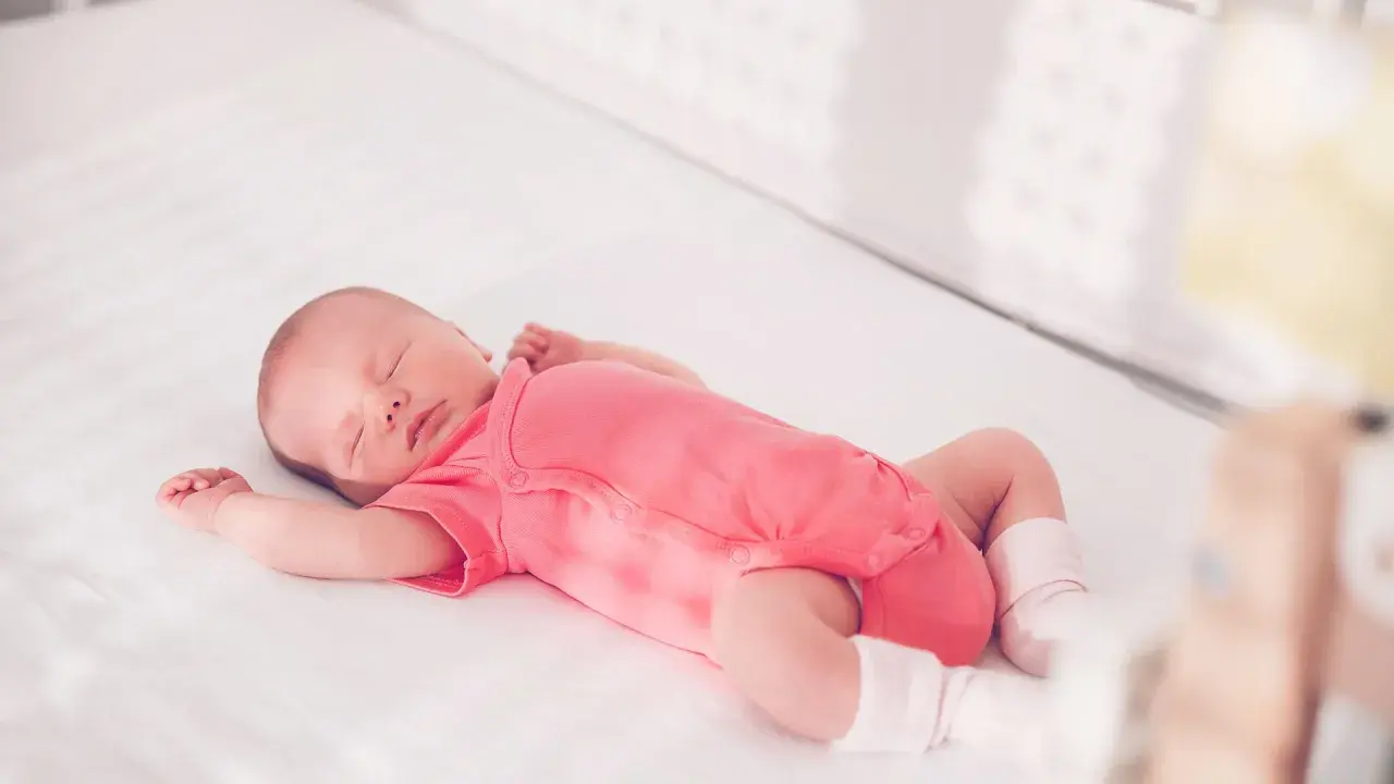 Ein schlafendes Baby in einem pinken Strampler streckt sich durch, während es in seinem Bettchen ruht.