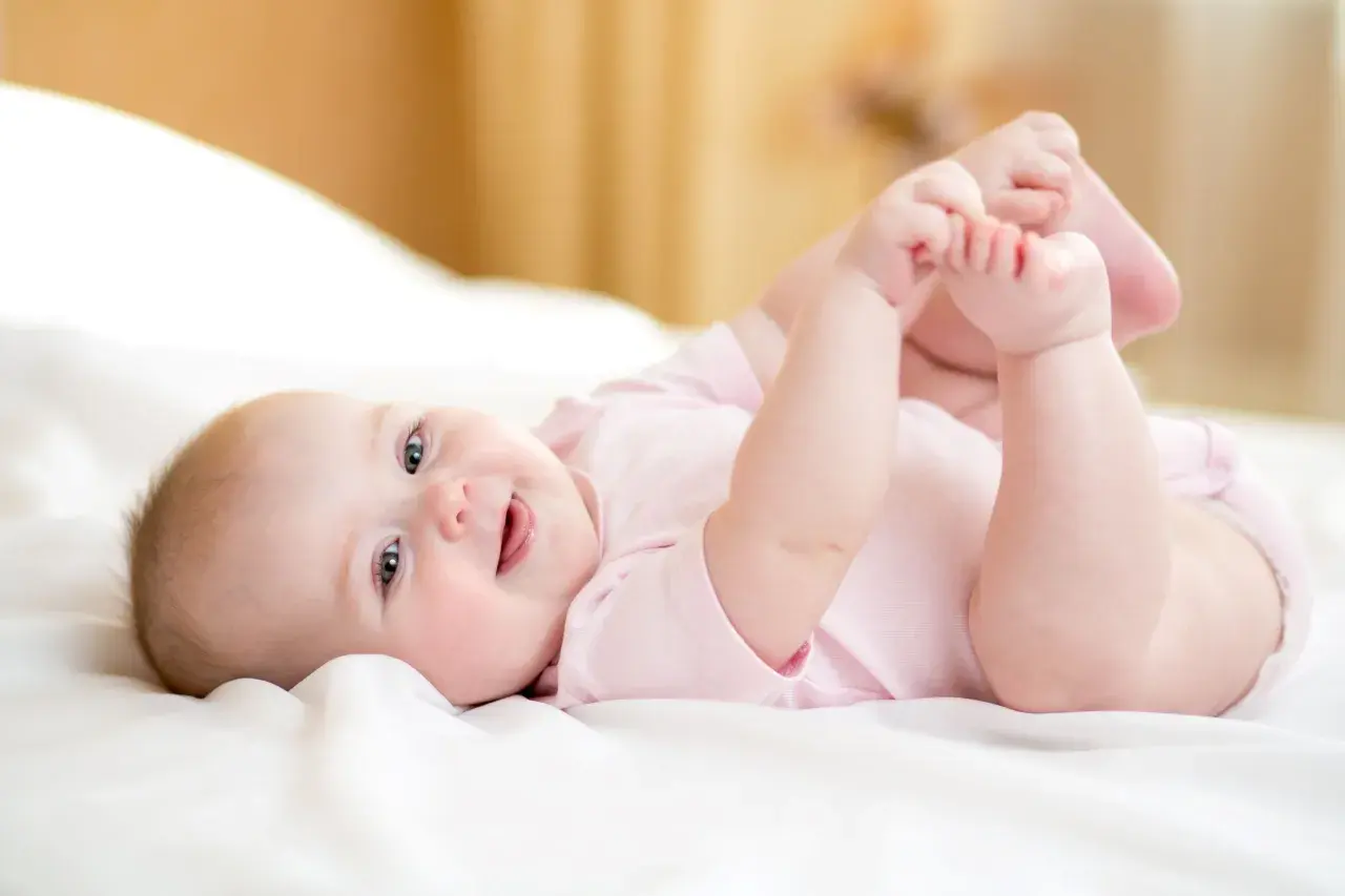 Ein lächelndes Baby von 8 Wochen liegt auf dem Rücken und spielt mit seinen Füßen.