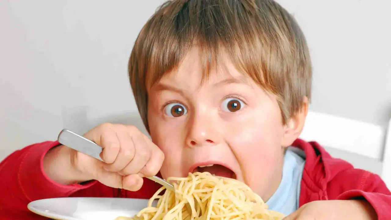 Junge isst mit großen Augen Spaghetti mit einer Gabel.