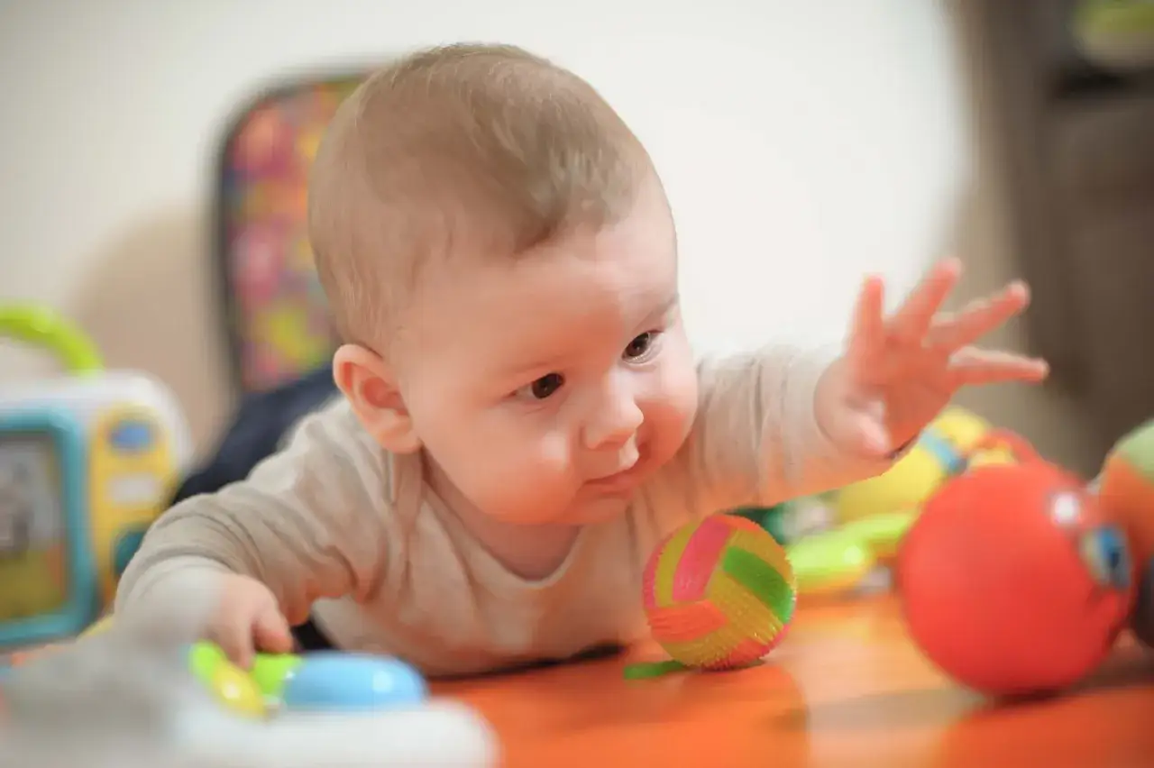 Baby krabbelt neugierig auf dem Bauch, greift nach bunten Spielsachen. Der 4 monats schub ist in vollem Gange!