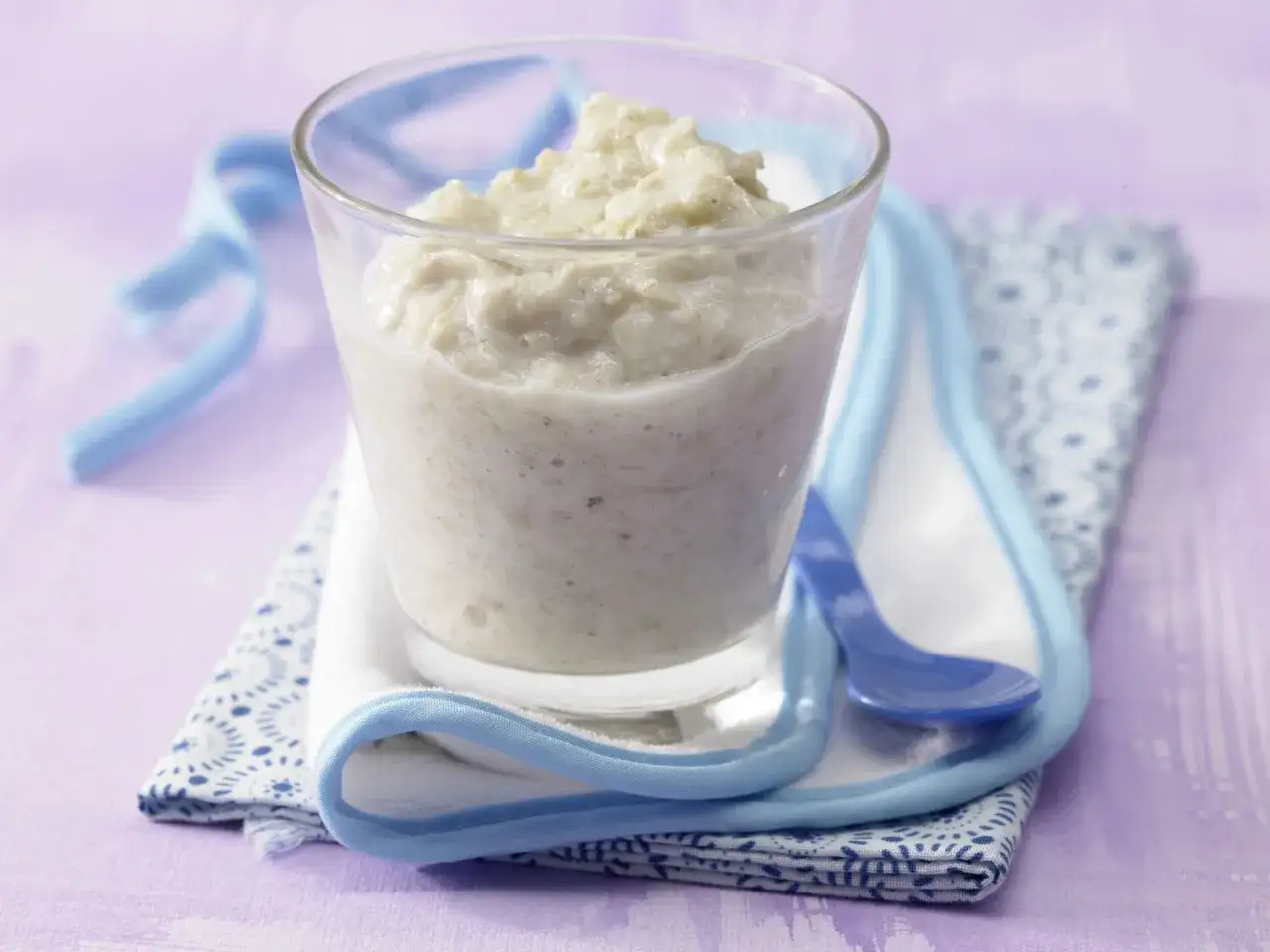 Ein Glas cremiger Brei, welcher Joghurt Baby k&ouml;nnte das sein? Daneben liegt ein blauer L&ouml;ffel und ein L&auml;tzchen.