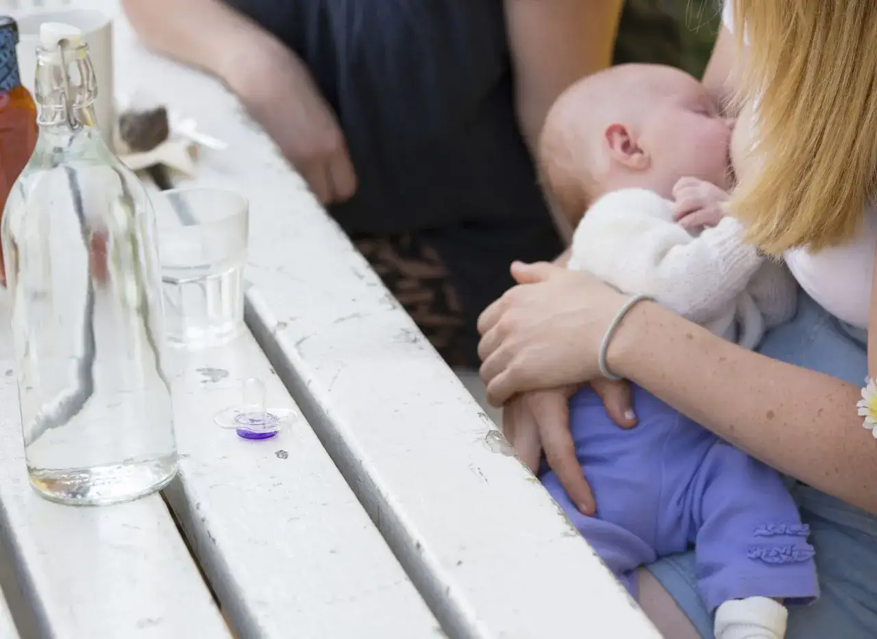 Mutter stillt ihr unruhiges Baby, w&auml;hrend auf dem Tisch ein Kaffee und eine Wasserflasche stehen.