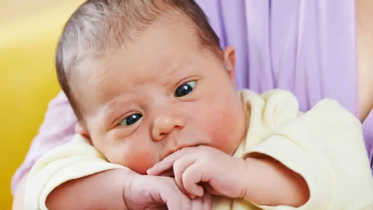 Ein s&uuml;&szlig;es Baby mit schielenden Augen liegt in den Armen seiner Mutter.