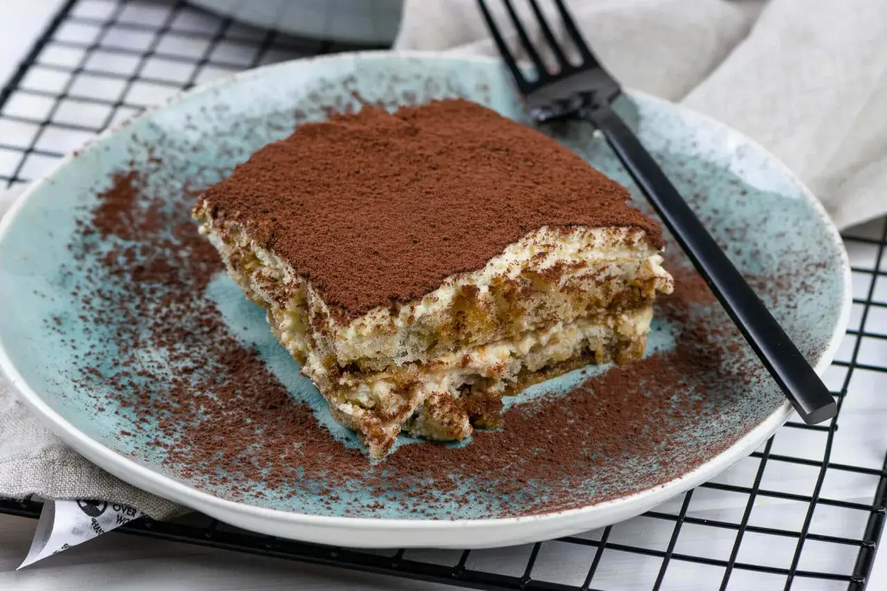 Ein St&uuml;ck Tiramisu, best&auml;ubt mit Kakao, auf einem blauen Teller. Perfekt f&uuml;r die Stillzeit, ein Genuss ohne Reue.