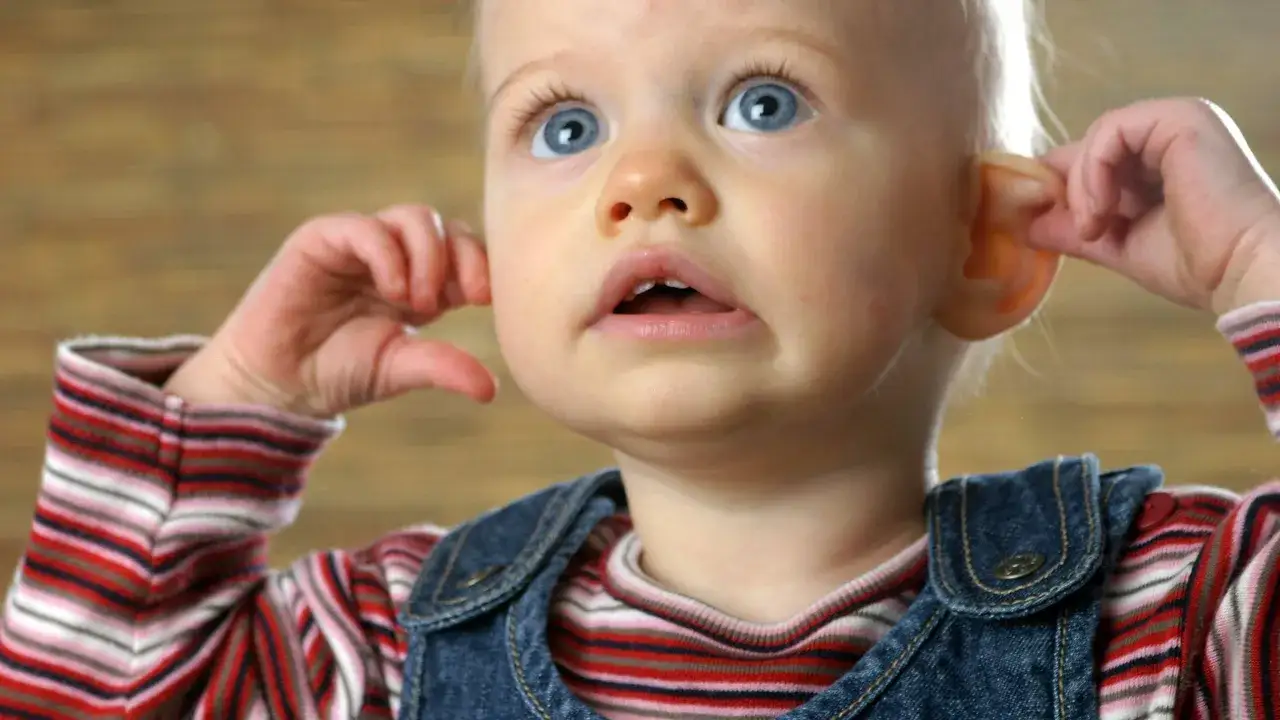 Ein Baby kratzt sich am Ohr, w&auml;hrend es neugierig in die Ferne blickt.