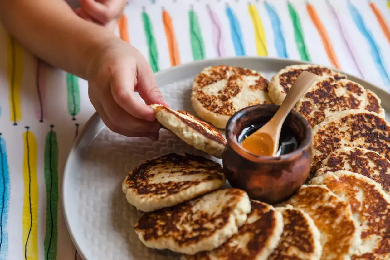 Kleiner Finger greift nach Pfannkuchen. Honigtopf mit L&ouml;ffel daneben. Perfekt f&uuml;r eine Beikost-Tabelle mit Lebensmitteln.