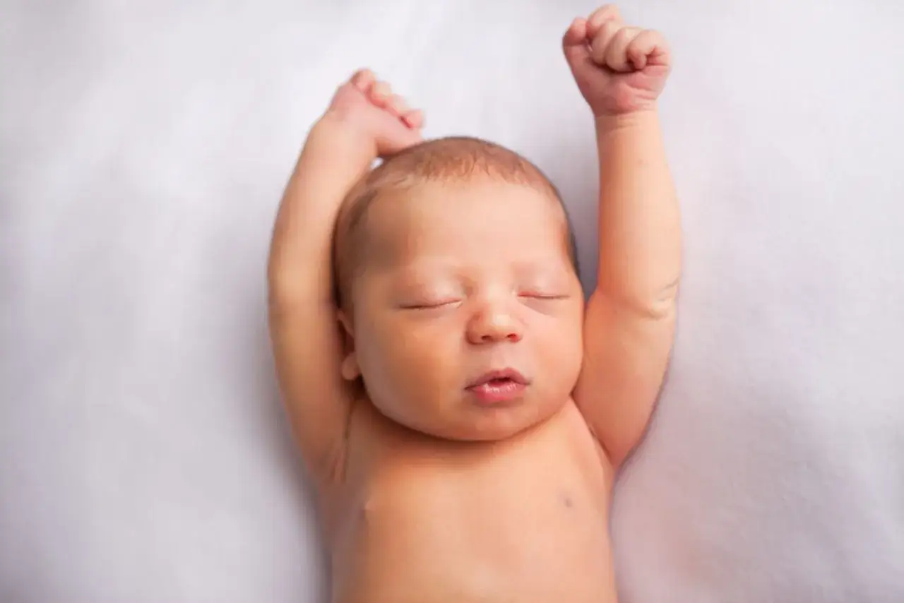 Ein Neugeborenes baby streckt sich durch, die Augen geschlossen, Arme nach oben erhoben.