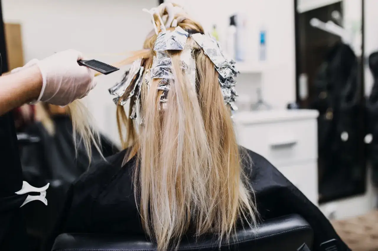 Friseur bearbeitet blonde Haare mit Folien. Die Stillzeit f&uuml;r das Blondieren beginnt.