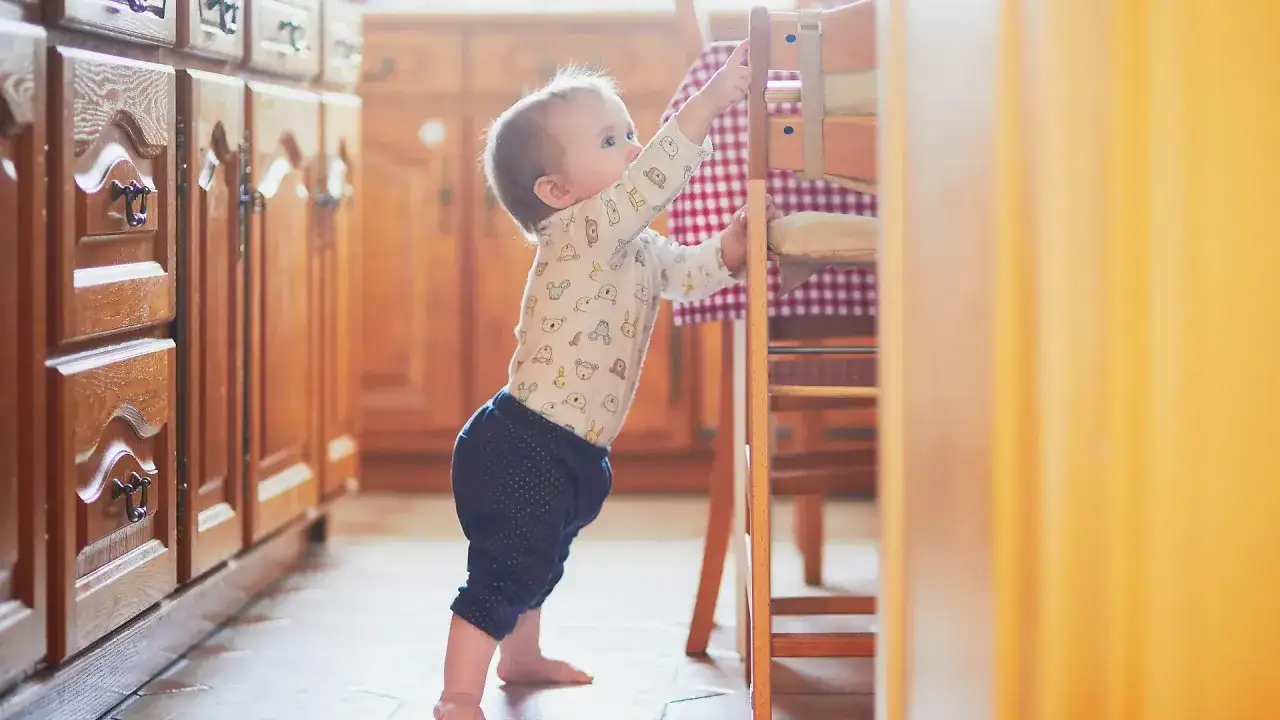 Baby steht an einem Hochstuhl und greift danach.