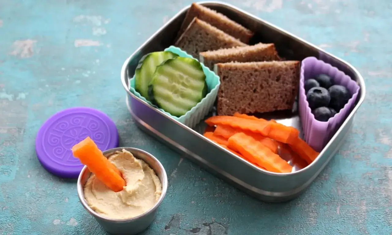 Gesunder Vesper f&uuml;r den Kindergarten: Vollkornbrot, Gurkenscheiben, Karottensticks mit Hummus und Blaubeeren.