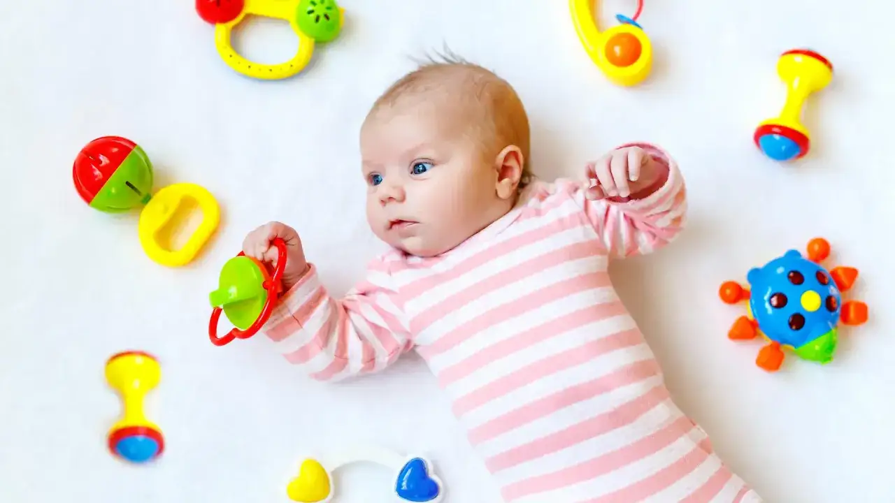 Baby in 12. Woche, umgeben von bunten Rasseln, erkundet neugierig seine Spielzeuge.