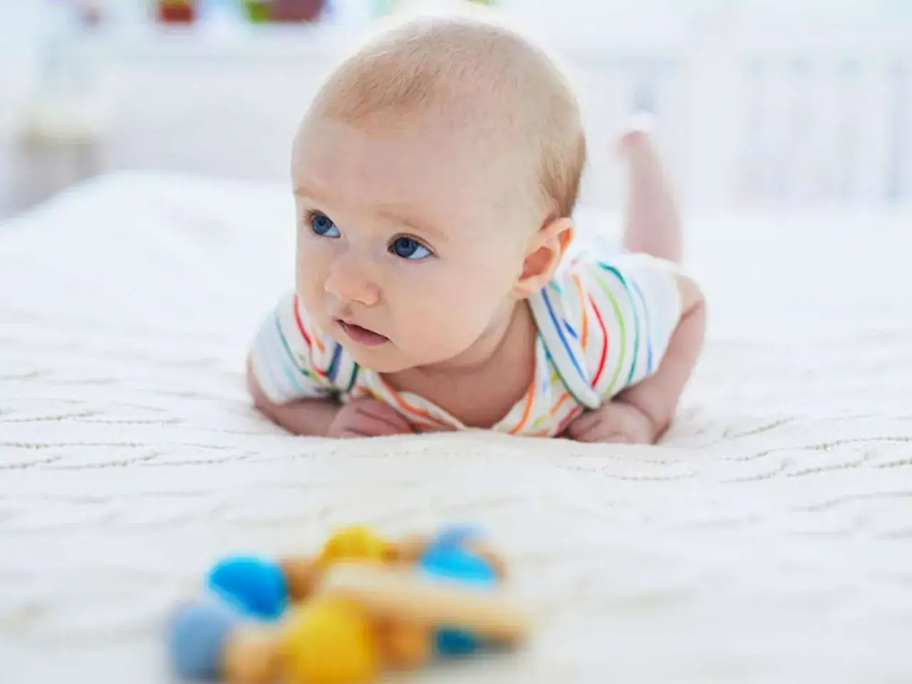 Ein s&uuml;&szlig;er baby 23 wochen alt liegt auf dem Bauch und schaut neugierig auf ein buntes Spielzeug.