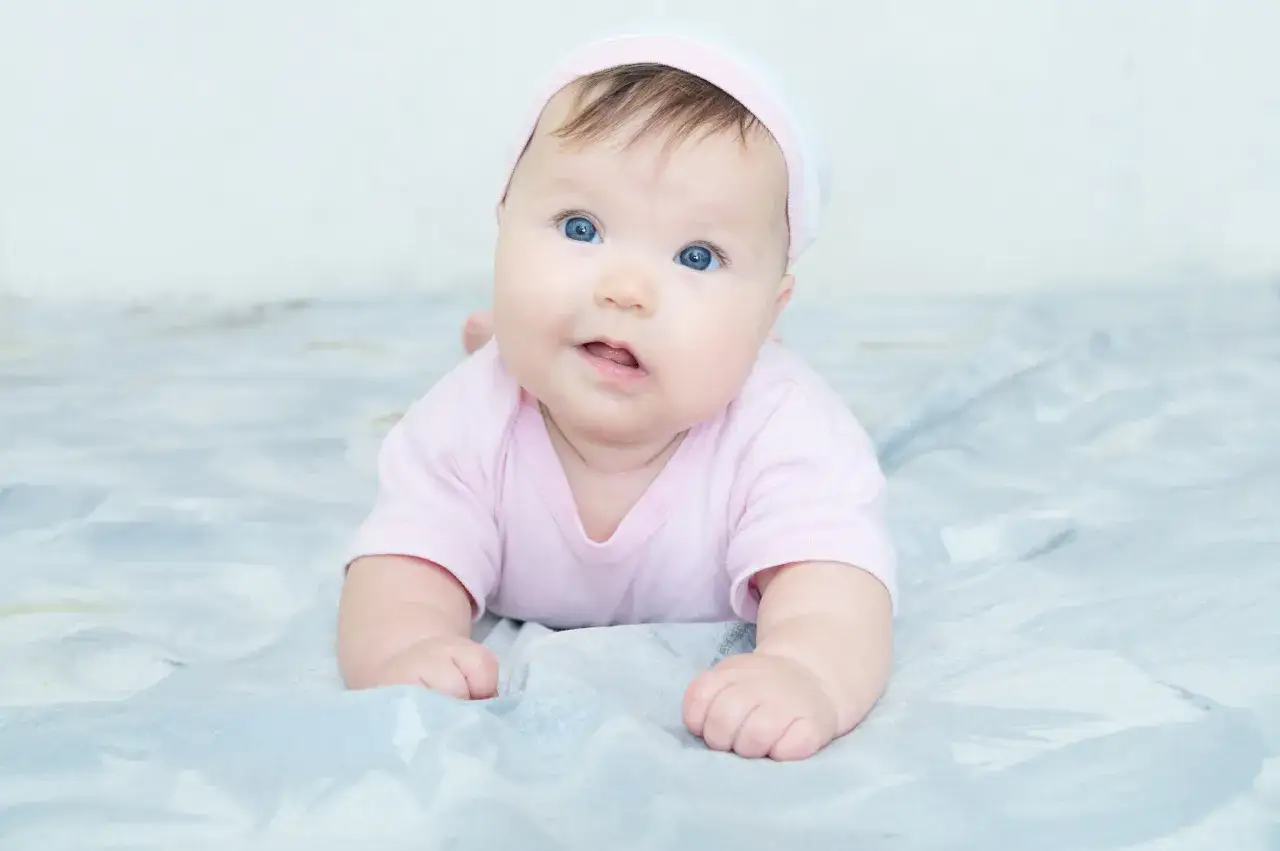 Blau&auml;ugiges Baby in rosa Strampler und M&uuml;tze liegt auf einer Decke. M&ouml;gliche kiss-syndrom symptome wie Kopfhaltung sind hier nicht erkennbar.